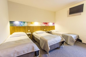 A hotel room with three single beds, a wooden headboard, a flat-screen TV mounted on the wall, and a geometric-patterned light fixture above the beds.