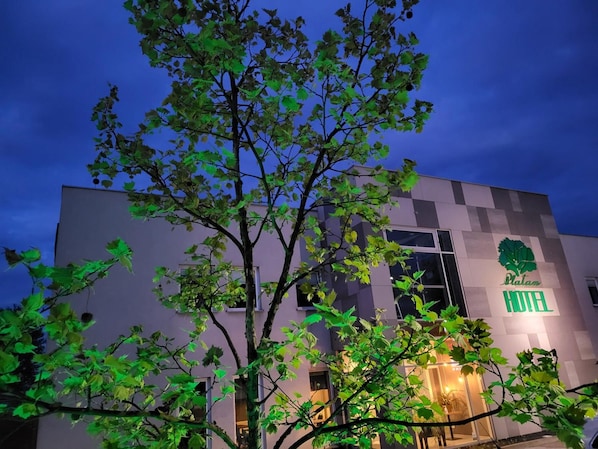 A modern hotel building with a visible tree logo and the name 'Platan Hotel' on the facade.