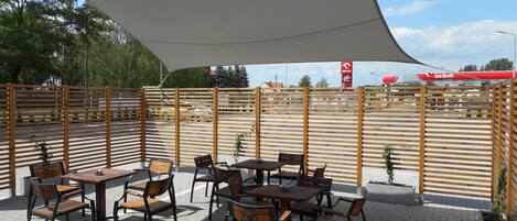 An outdoor patio area with tables and chairs, a large canopy, and a wooden fence.