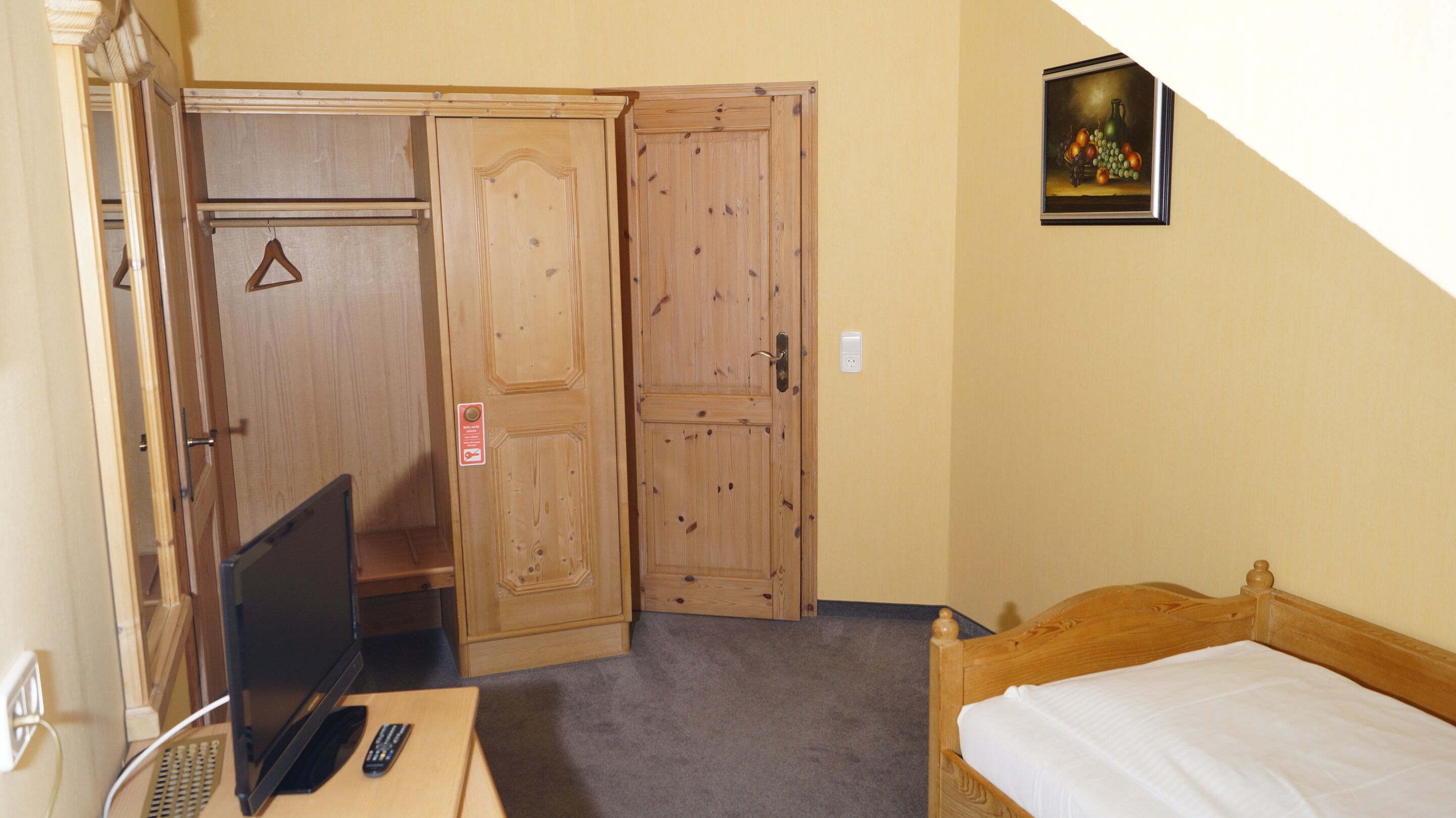 A room with a bed, a desk with a computer, a TV, and wooden wardrobes.