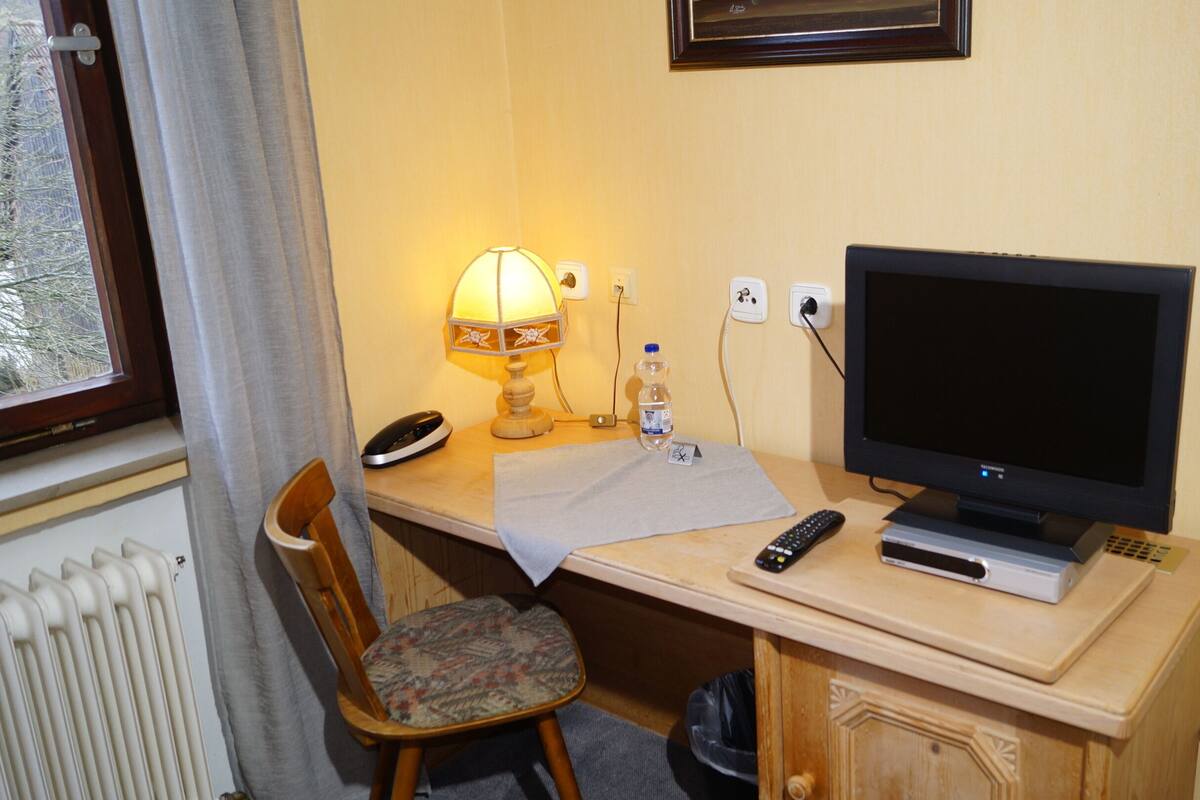 Habitación de hotel con escritorio de madera, televisor, lámpara, silla y radiador.