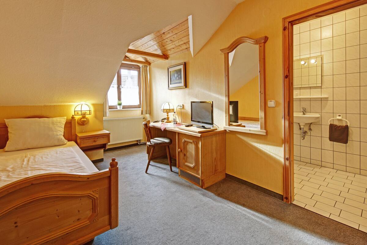 Un dormitorio con cama, escritorio, silla y baño con pared y puerta de azulejos.