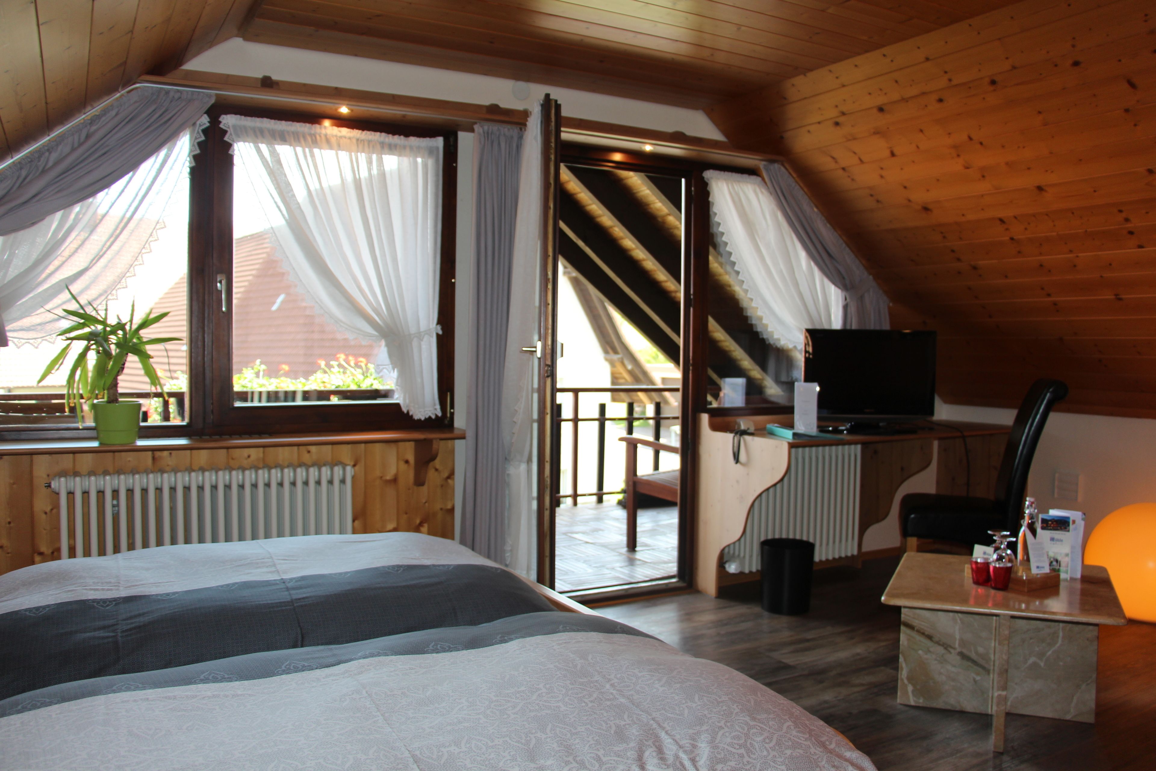 Ein Schlafzimmer mit Bett, Schreibtisch mit Computer, Stuhl und Balkon mit Blick ins Freie.