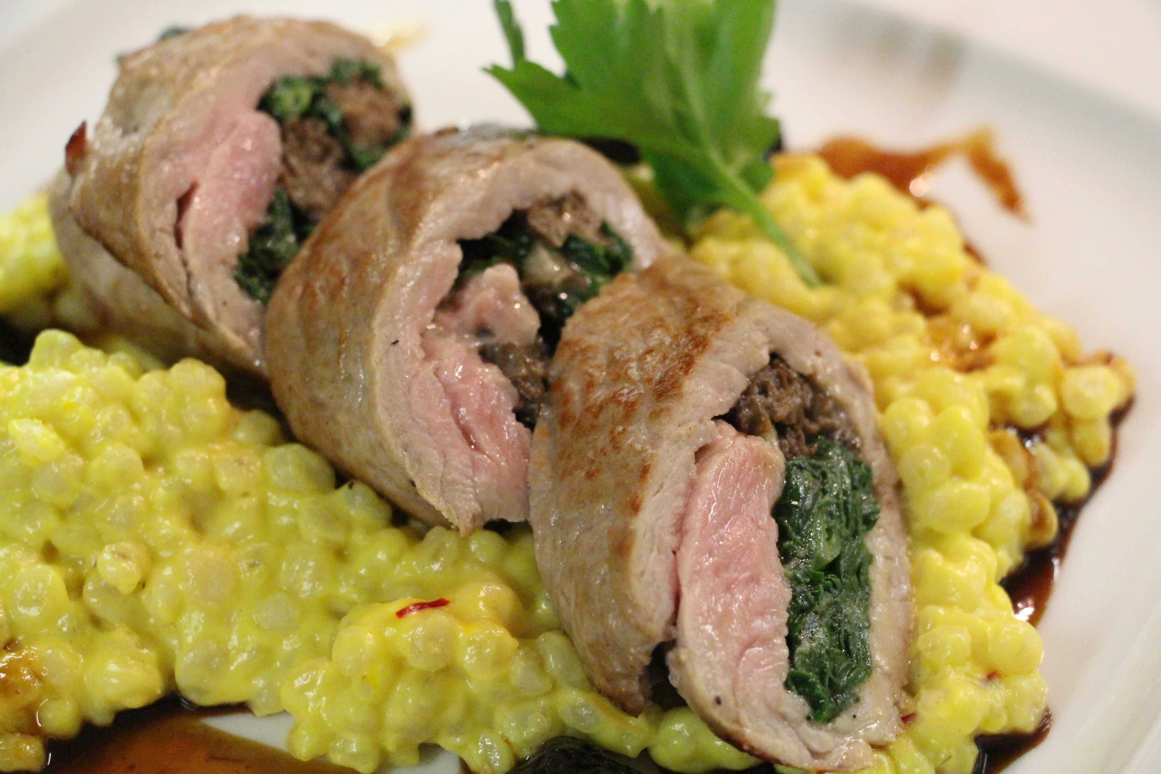 A dish with rolled meat and spinach, served with yellow risotto.