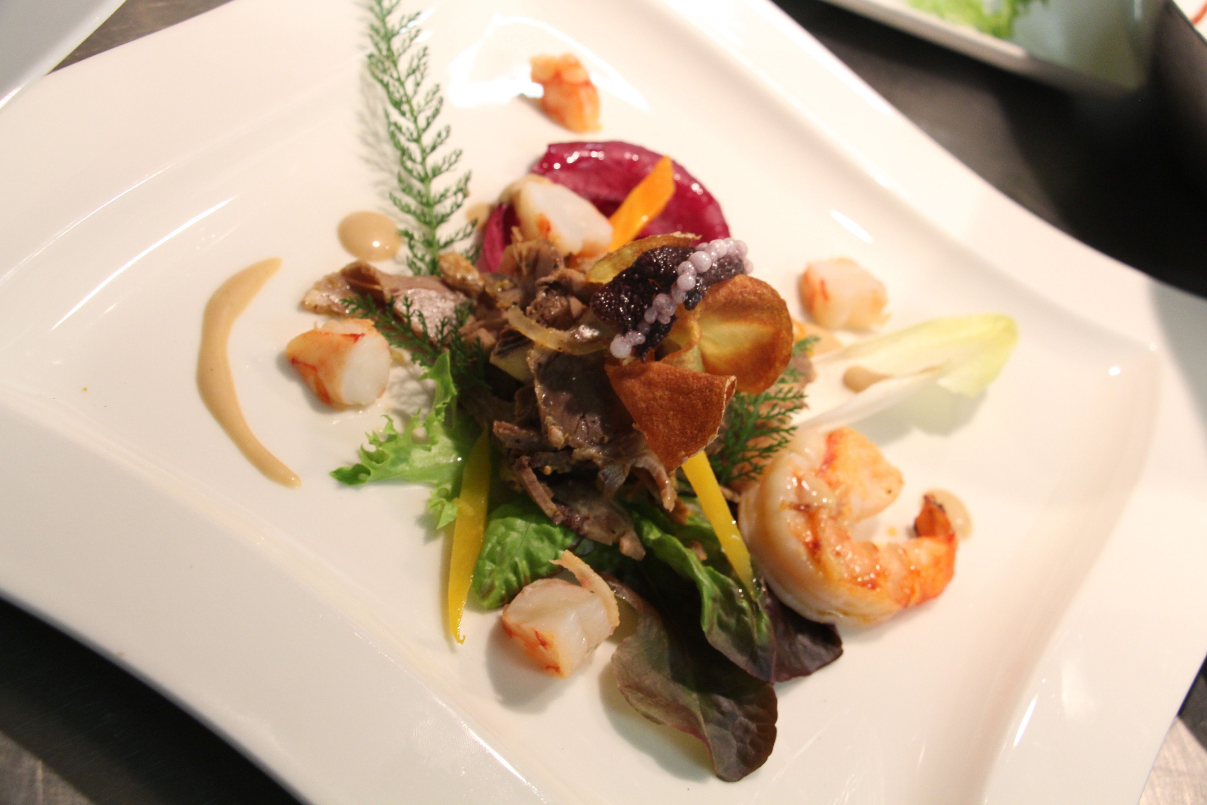 Un plato blanco con un guiso de mariscos, incluyendo camarones y verduras, además de una remolacha roja.