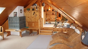 An attic room with wooden beams, a fireplace, wicker furniture, and a small table with a bottle and glasses.