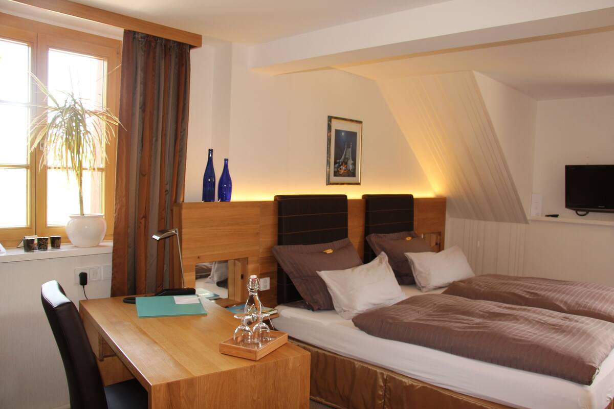 Een hotelkamer met een bed, nachtkastje, lamp en een raam met gordijnen.