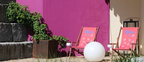 A patio area with two red lounge chairs, a white globe, and a potted plant.