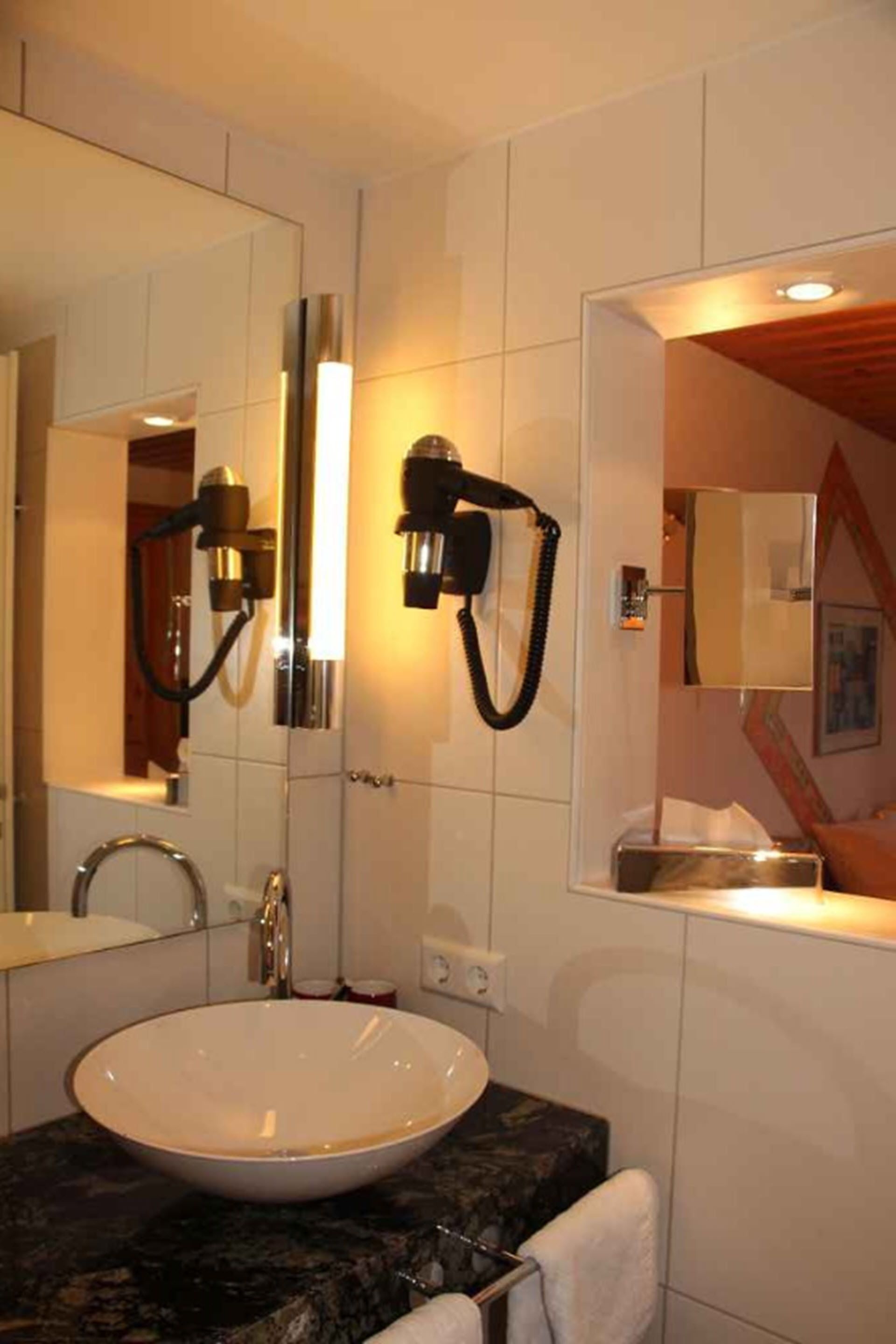 A modern bathroom with a white sink, a large mirror, and two wall-mounted hair dryers.