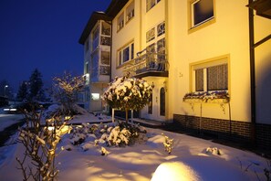 A multi-story building with balconies, a snow-covered ground, and a lit exterior.