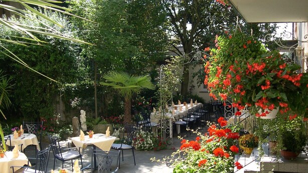 An outdoor dining area with tables and chairs, surrounded by lush greenery and flowering plants. - Hotel Anika (Neuenburg am Rhein)