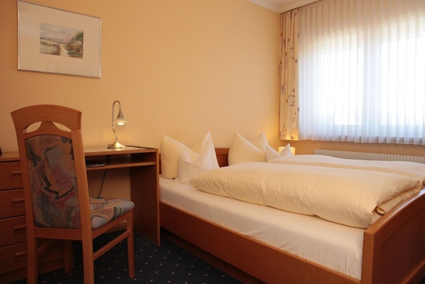 A hotel room with a bed, desk, chair, and a painting on the wall.