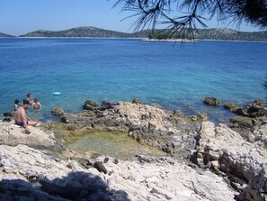 A rocky shoreline with clear blue water and a few people in the water. - Marvie apartmani (Primosten)