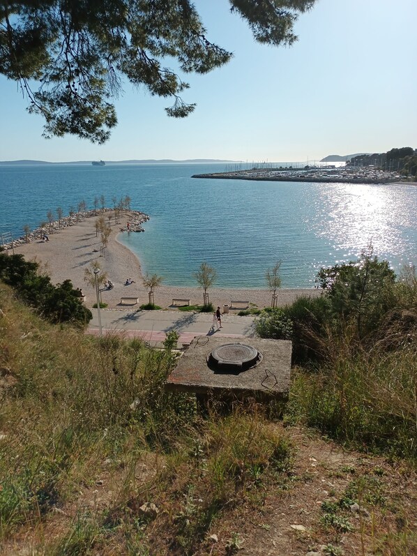 A coastal promenade with a stone pathway, benches, and a circular structure.