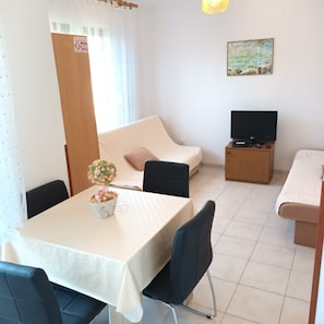 A compact living space with a dining table, a sofa, a TV stand, and a painting on the wall.