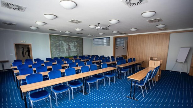 A conference room with rows of blue chairs, wooden tables, and a whiteboard. - Hotel Grand (Hradec Kralove)
