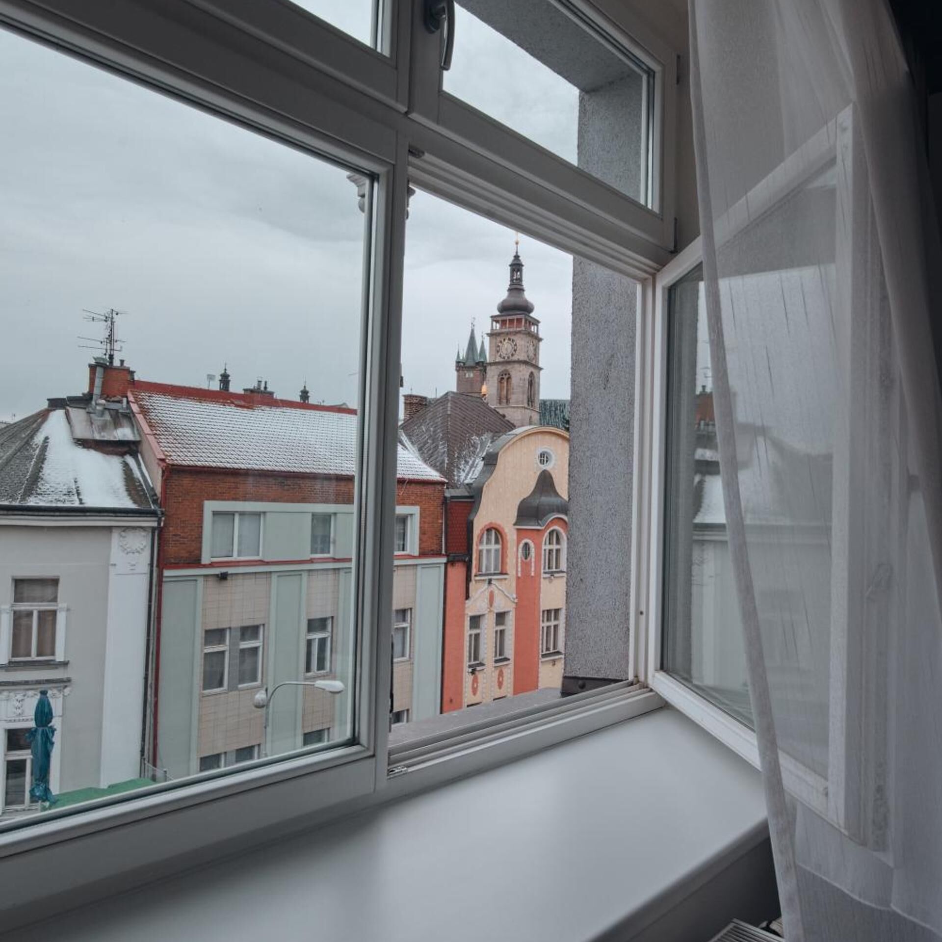 Una ventana con vistas a edificios, incluyendo una torre con reloj.