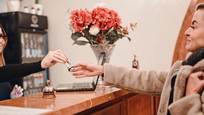 A reception desk with a laptop, a vase of flowers, and a wooden counter. - Hotel Grand (Hradec Kralove)