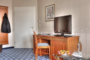 Habitación de hotel con escritorio de madera, una silla, un televisor, una mesita con frutero y una botella de agua.