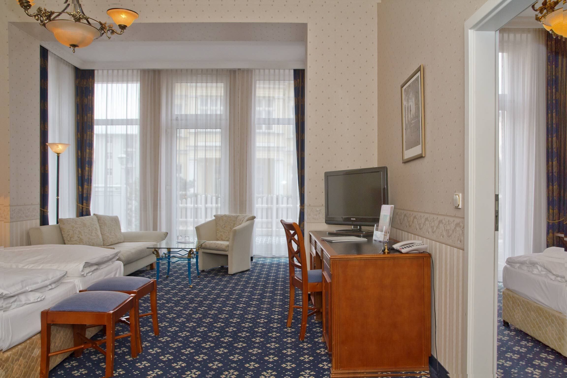 A hotel room with a bed, a desk with a chair, a television, and a window with curtains.