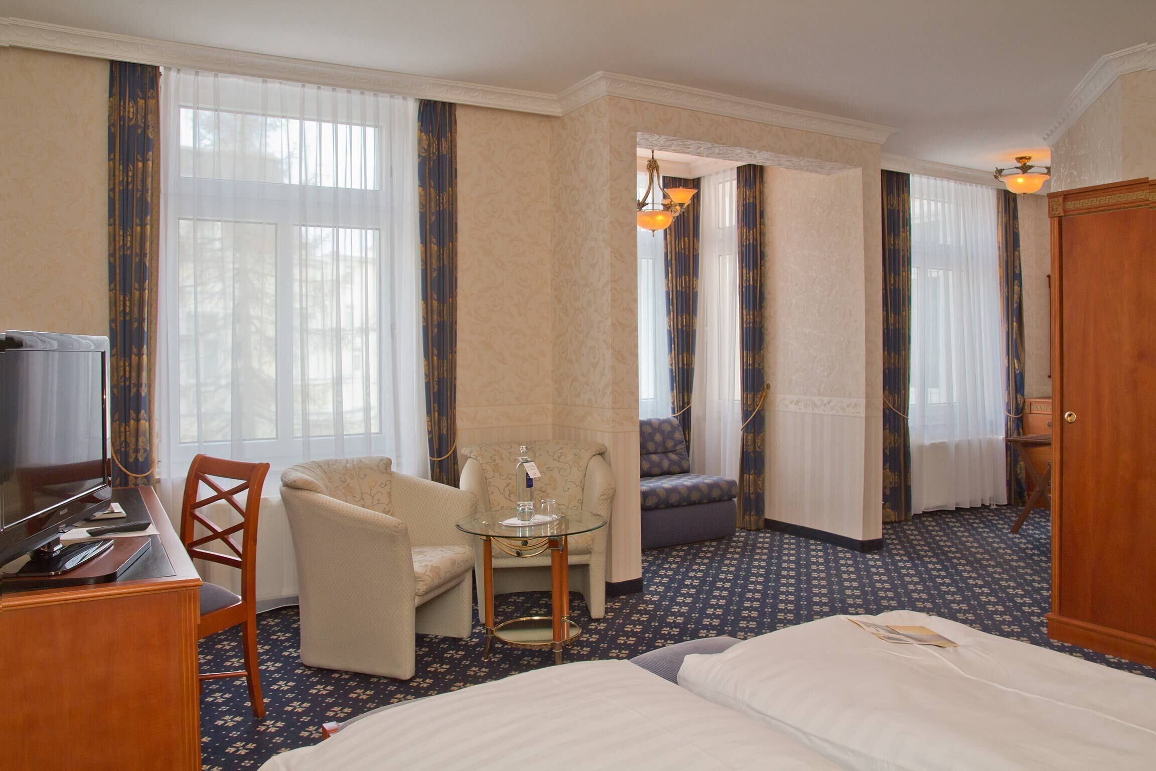 A hotel room with a bed, a desk with a computer, a chair, a small table, and a television.