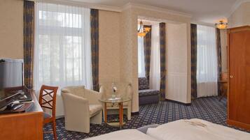 A hotel room with a bed, a desk with a computer, a chair, a small table, and a television.