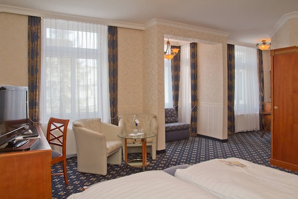 Habitación de hotel con una cama, un escritorio con computadora, una silla, una mesita y un televisor.