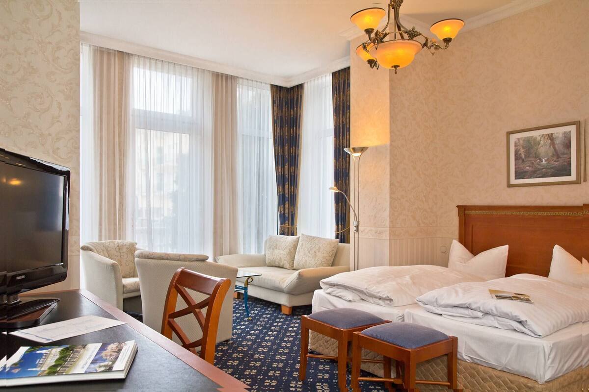 Une chambre d’hôtel avec un lit, un bureau avec une télévision, une chaise, un canapé et une grande fenêtre avec des rideaux.