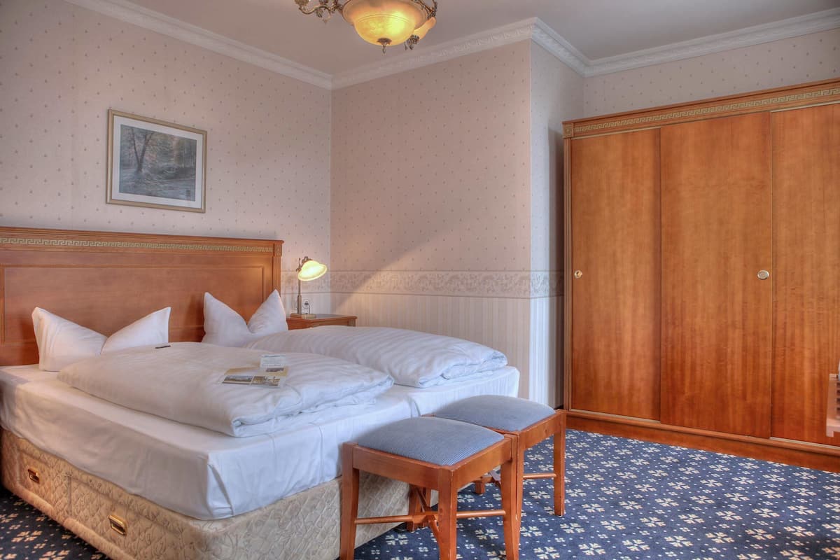 Une chambre d’hôtel avec un grand lit, une armoire en bois, un tableau encadré au mur et une moquette à motifs.
