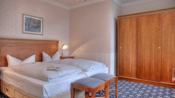 A hotel room with a large bed, a wooden wardrobe, a framed picture on the wall, and a patterned carpet.