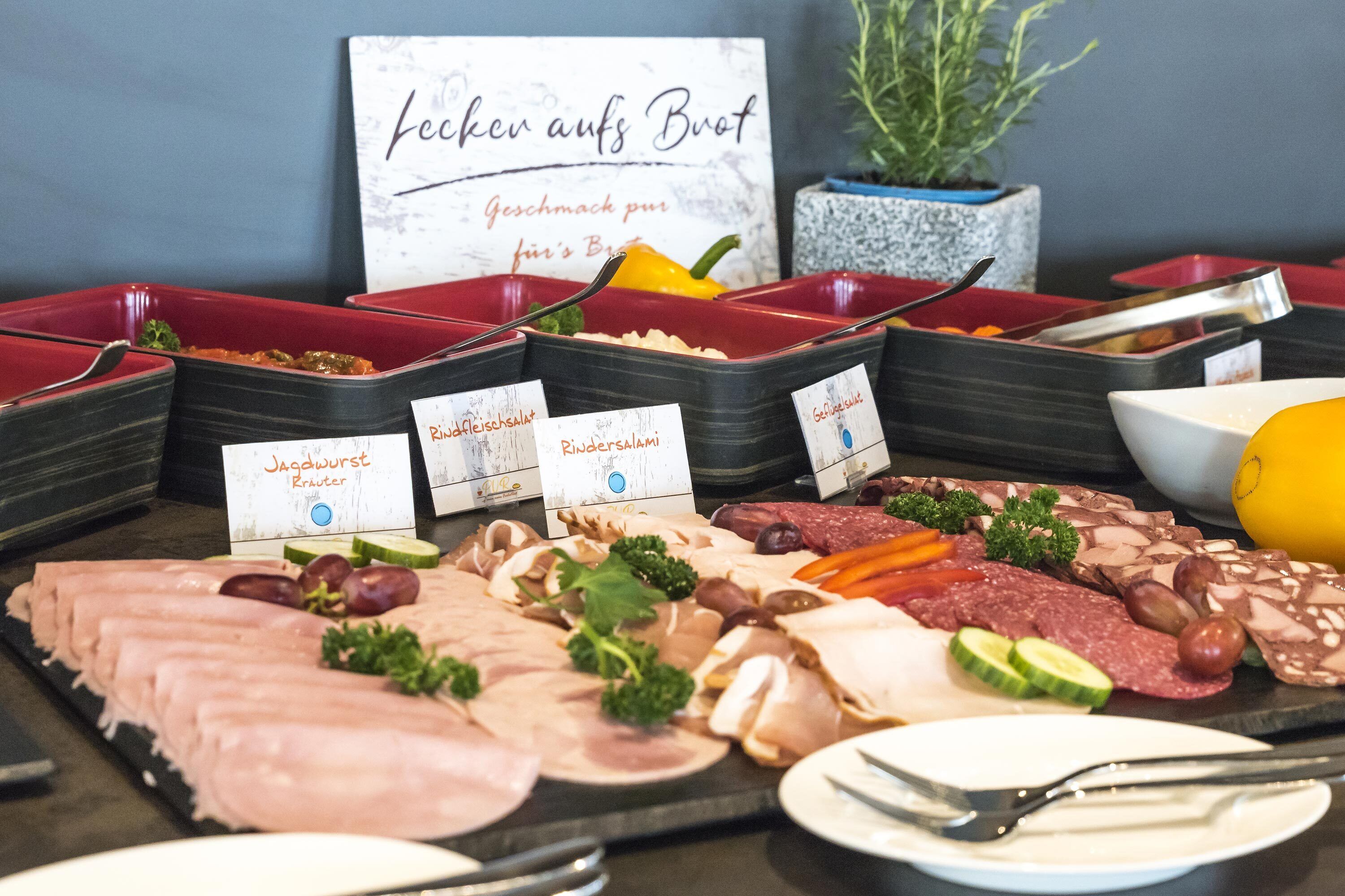 A buffet with various meats and vegetables, including ham, salami, and cucumbers, with labels in a foreign language.
