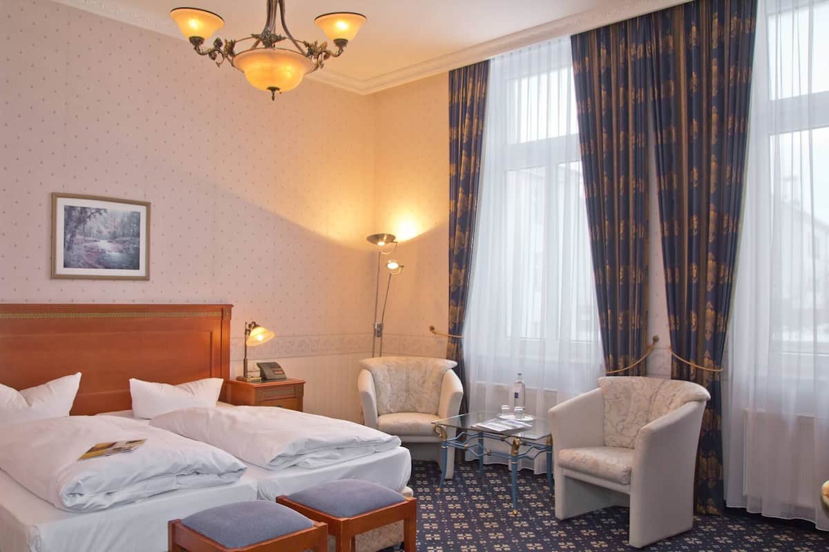 Une chambre d’hôtel avec un lit double, deux fauteuils, une petite table, une lampe et un tableau au mur.