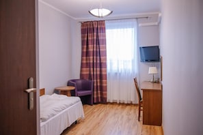 A hotel room with a bed, a desk with a lamp, a chair, a television, and a window with curtains.