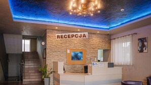 A reception area with a stone wall, a reception desk, a clock, and a staircase. - Zajazd Blue (gmina Stare Miasto)