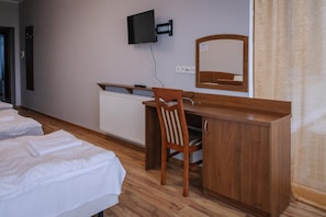A hotel room with a wooden desk, a chair, a television mounted on the wall, a mirror, and two beds.