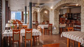 A restaurant with multiple tables and chairs, stone walls, and a view of the city.