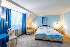 A bedroom with a bed, a chair, a table, and a window with curtains. - Hotel Trumf (Mlada Boleslav)