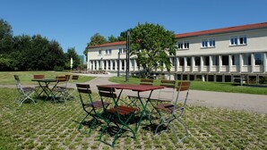 A building with a red roof, multiple windows, and a paved area with outdoor seating. - Tagungshaus Regina Pacis (Leutkirch im Allgau)
