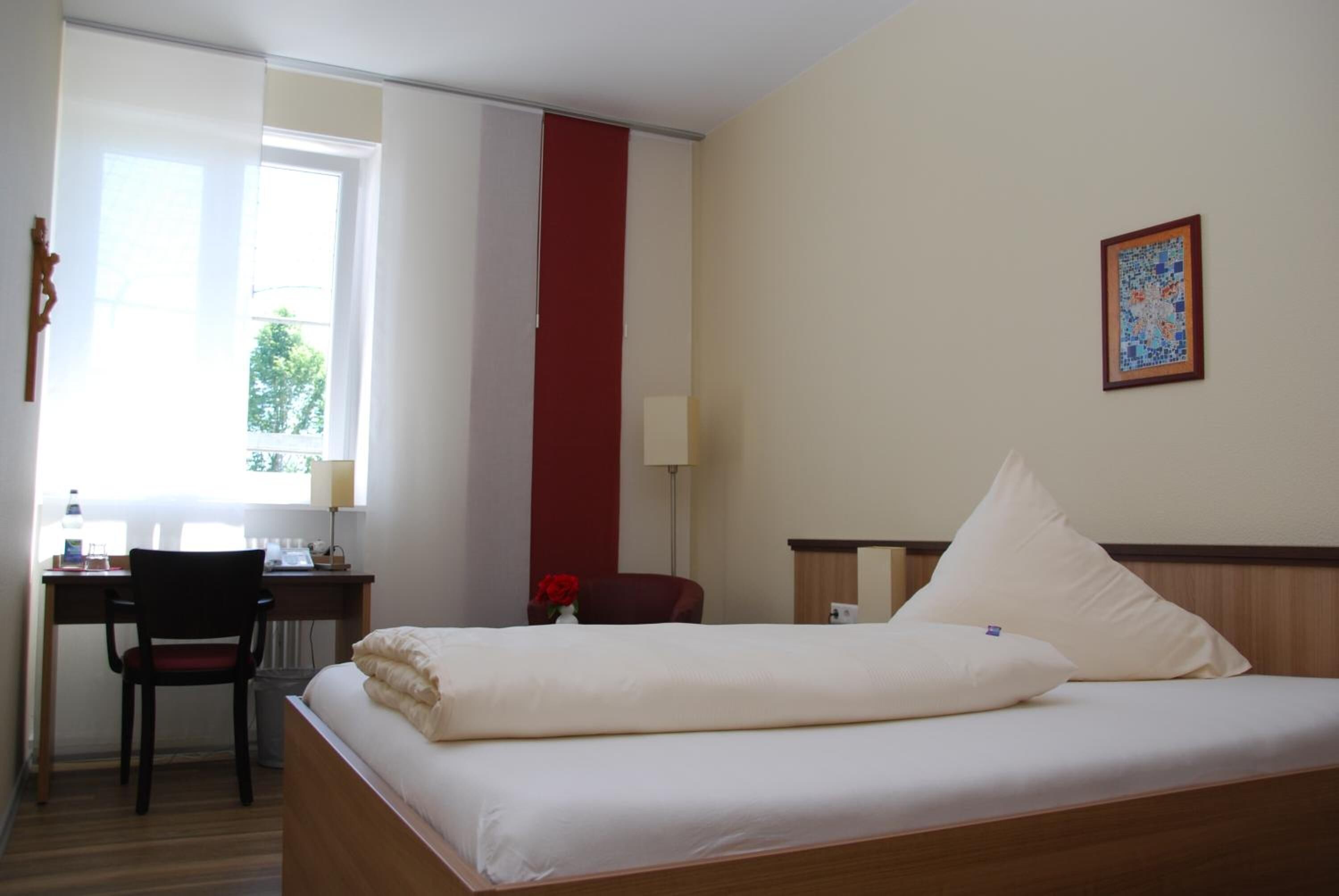 Hotelkamer met een bed, bureau, stoel en een raam met uitzicht op bomen.