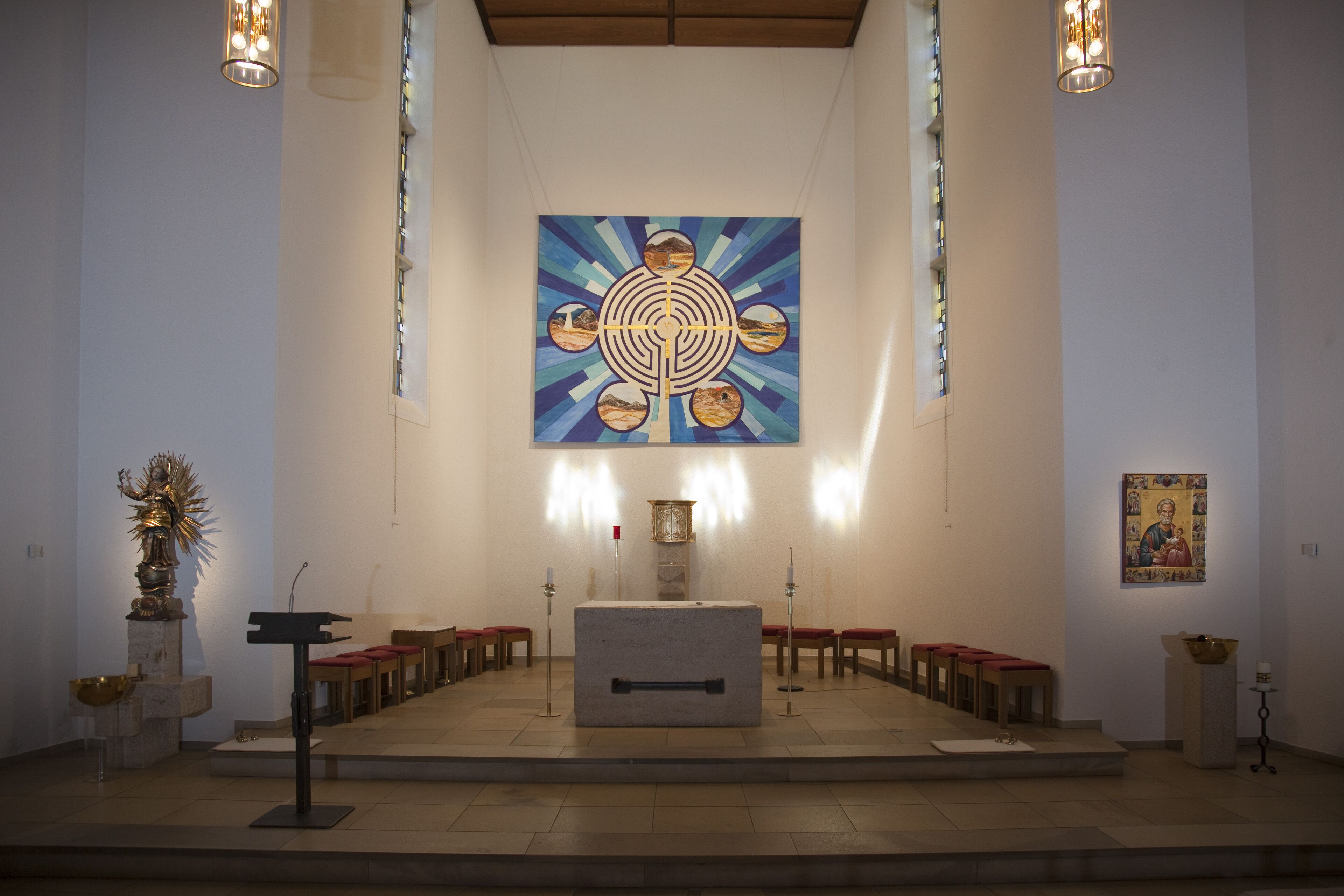Interior de iglesia con altar central, bancas y un gran cuadro religioso en la pared.