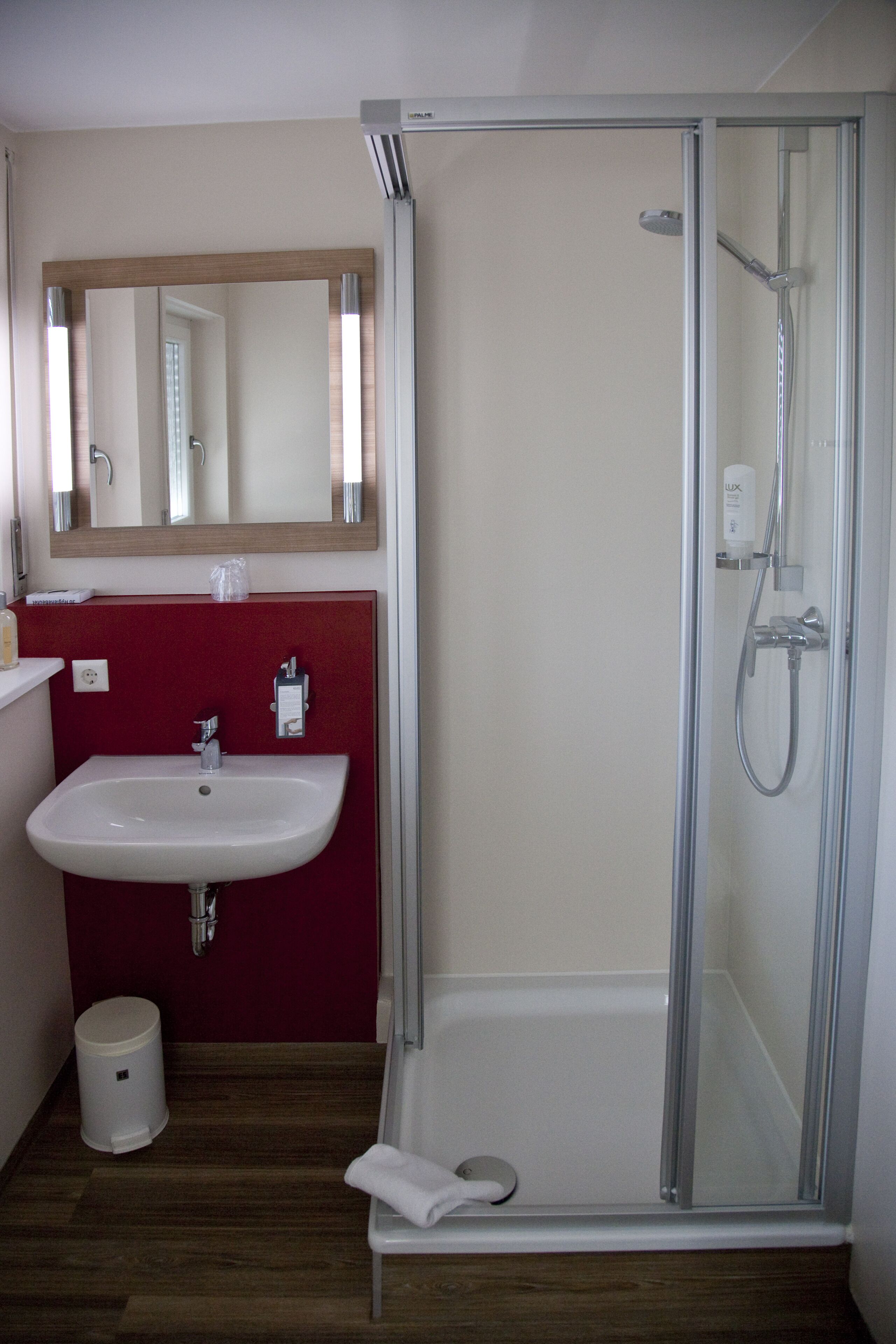 A bathroom with a glass-enclosed shower, a white sink, and a red accent wall.