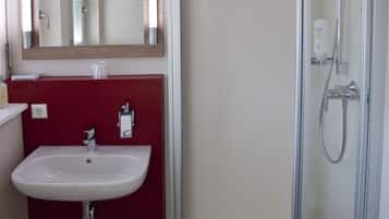 A bathroom with a glass-enclosed shower, a white sink, and a red accent wall.