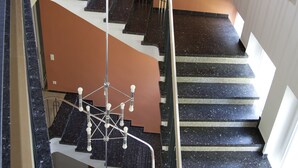 A multi-level interior with a central staircase, metal railings, and a hanging light fixture. - Tagungshaus Regina Pacis (Leutkirch im Allgau)