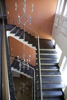 Un interior de varios niveles con una escalera central, barandillas de metal y una lámpara colgante.