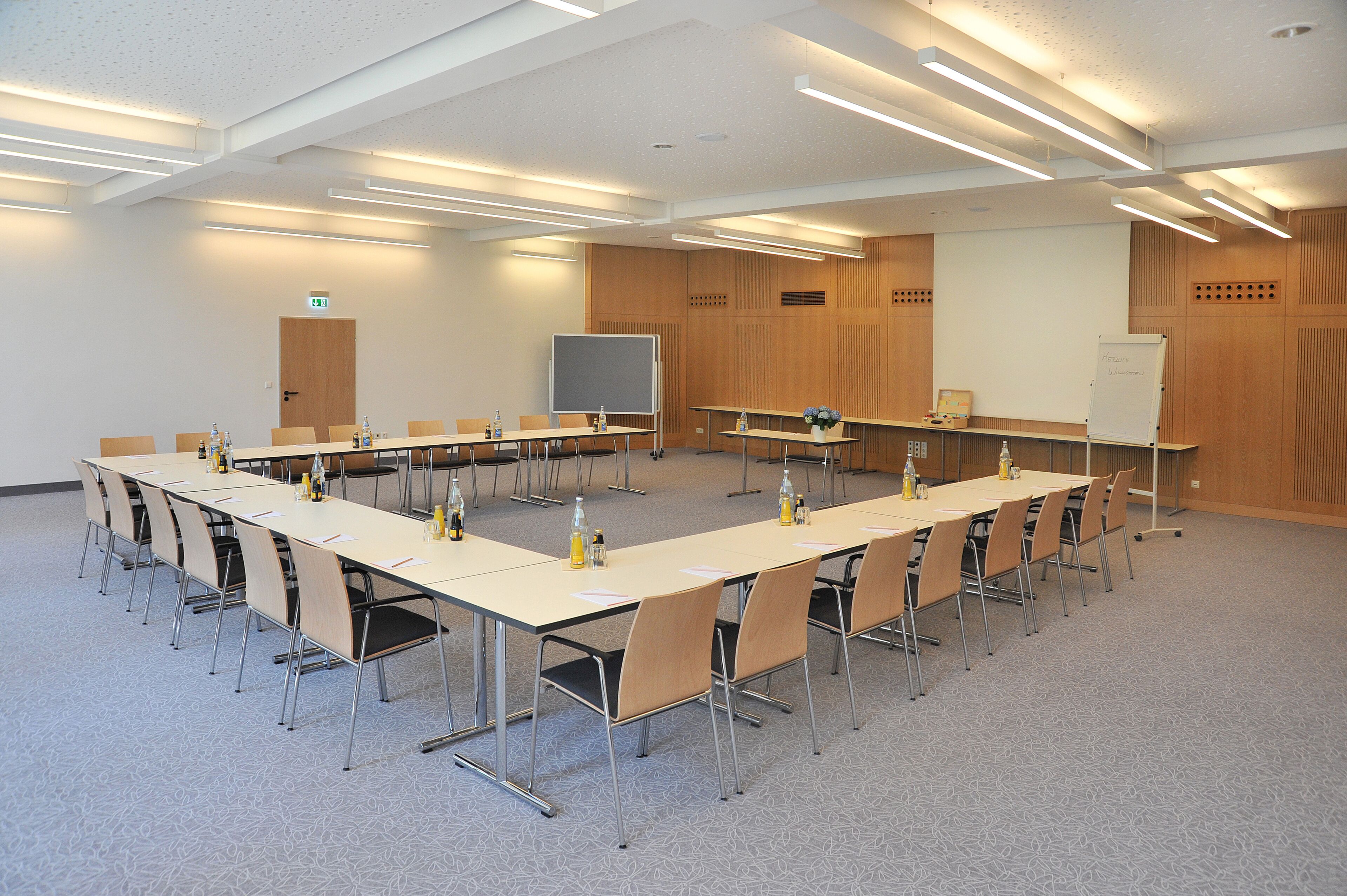 A conference room with long tables, chairs, a whiteboard, and a projector screen.