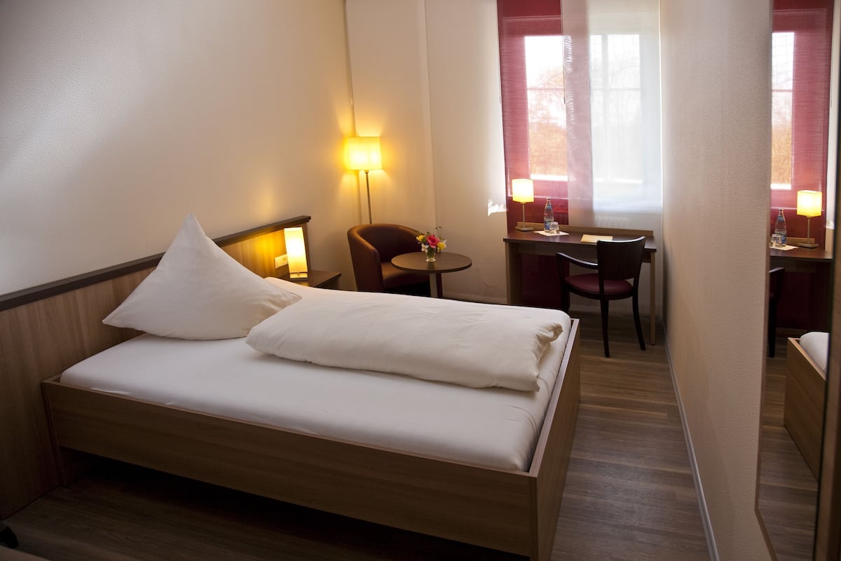 A hotel room with a wooden bed, a desk, a chair, and two lamps.