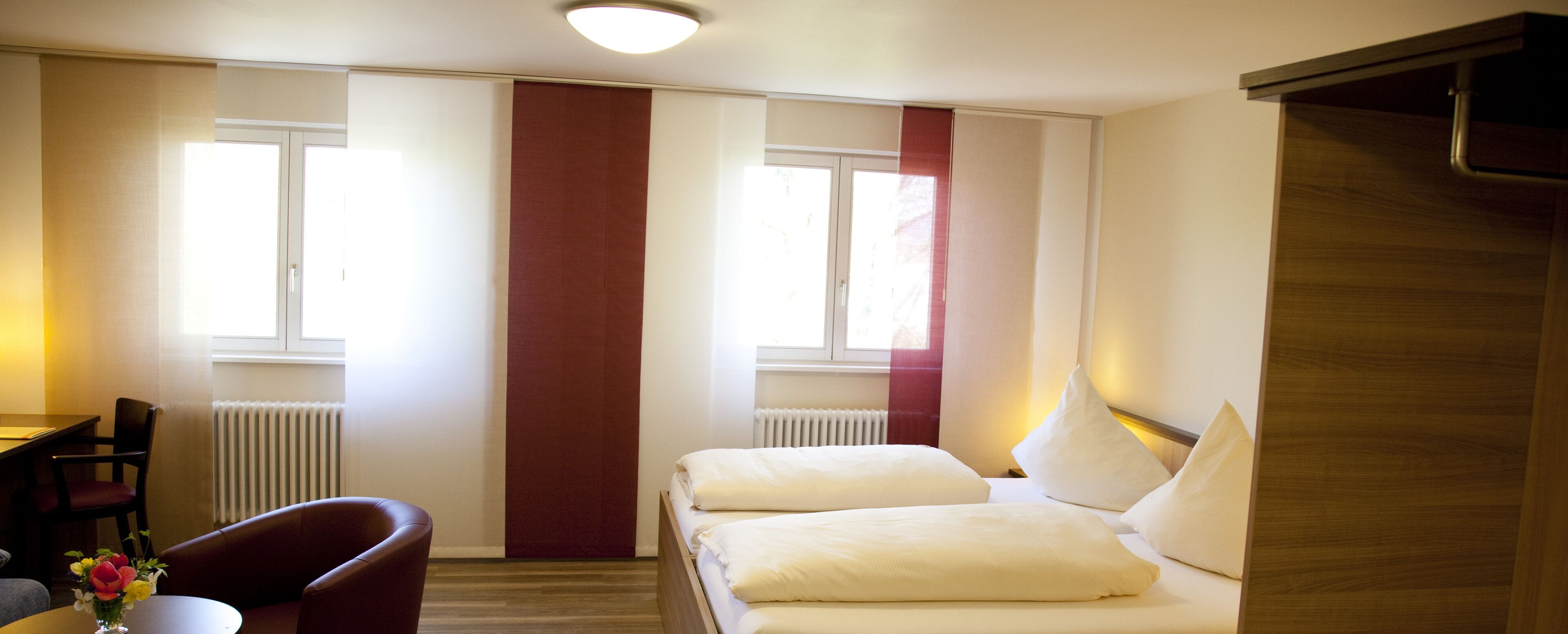 Una habitación de hotel con cama, una silla, una mesa y un florero con flores.