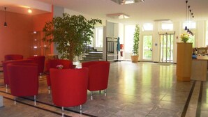 A spacious lobby with red seating, a staircase, and a reception desk. - Tagungshaus Regina Pacis (Leutkirch im Allgau)