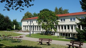 A building with a red roof, surrounded by a well-maintained lawn and benches. - Tagungshaus Regina Pacis (Leutkirch im Allgau)