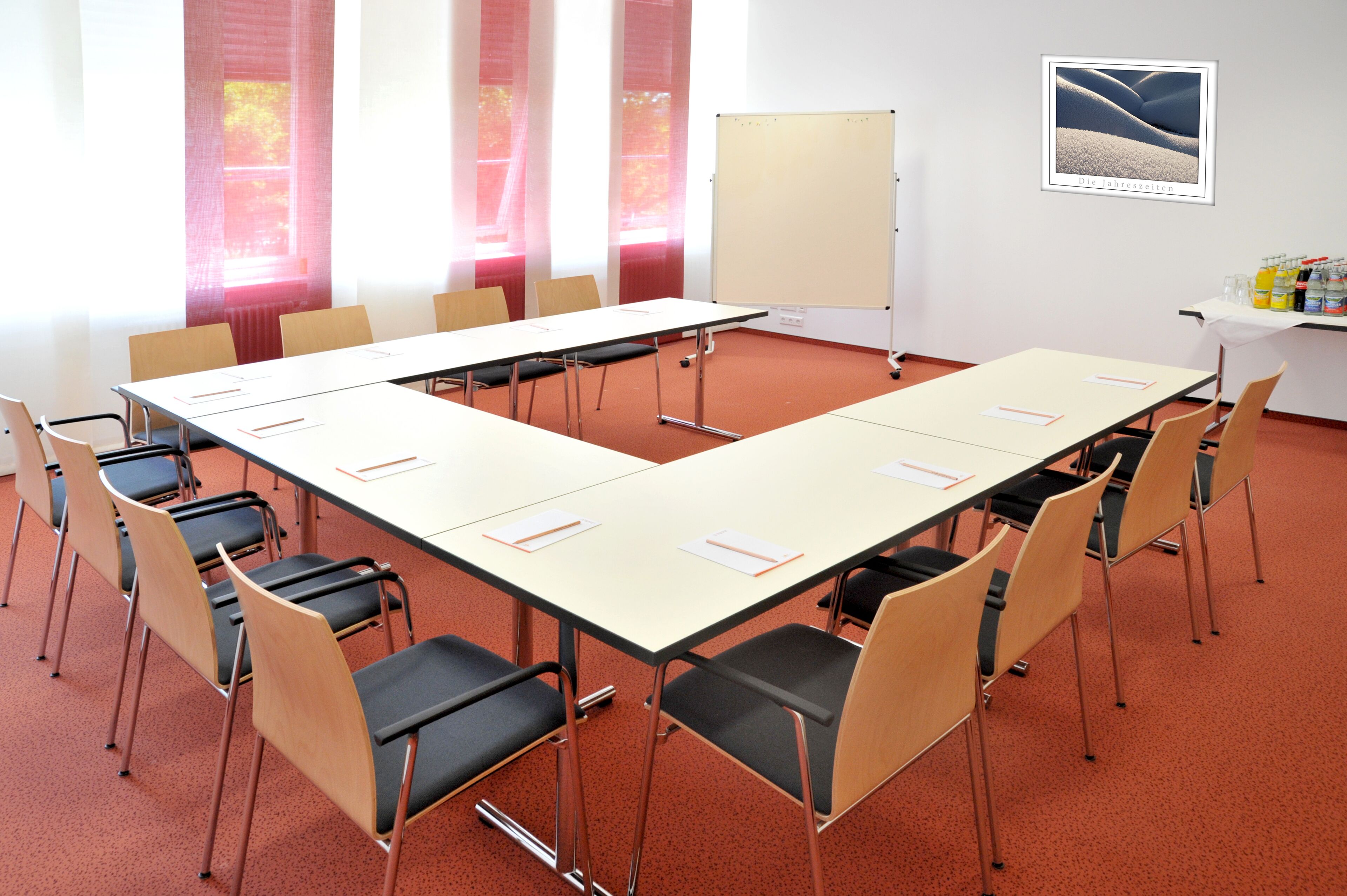Ein Konferenzraum mit langem Tisch, Stühlen, einer Whiteboard und einem gerahmten Bild an der Wand.